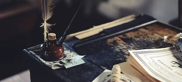 An inkwell, pen and open ledger on a worn wooden desk.